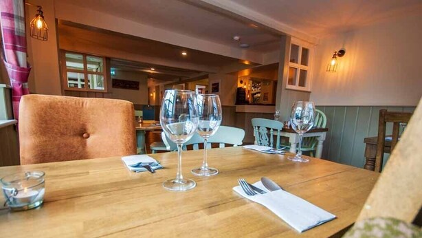 A dining table set with wine glasses, a candle, and cutlery in a cozy restaurant setting. - The White Lion (Ventnor)