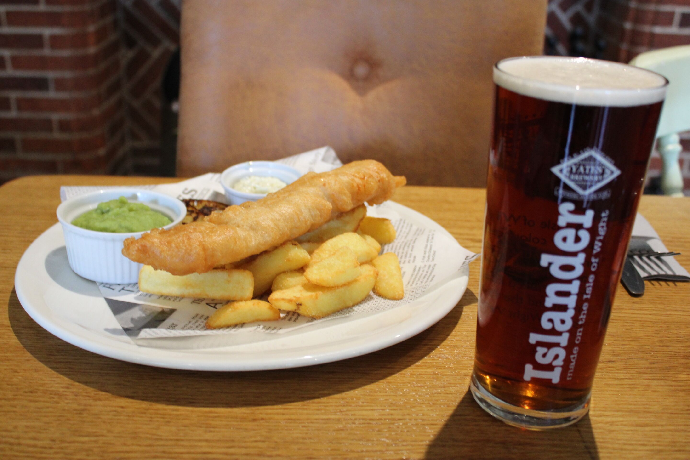 A plate of fish and chips with a glass of beer on a wooden table.