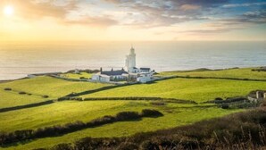 A coastal lighthouse with a white tower, surrounded by green fields and a clear sky. - The White Lion (Ventnor)