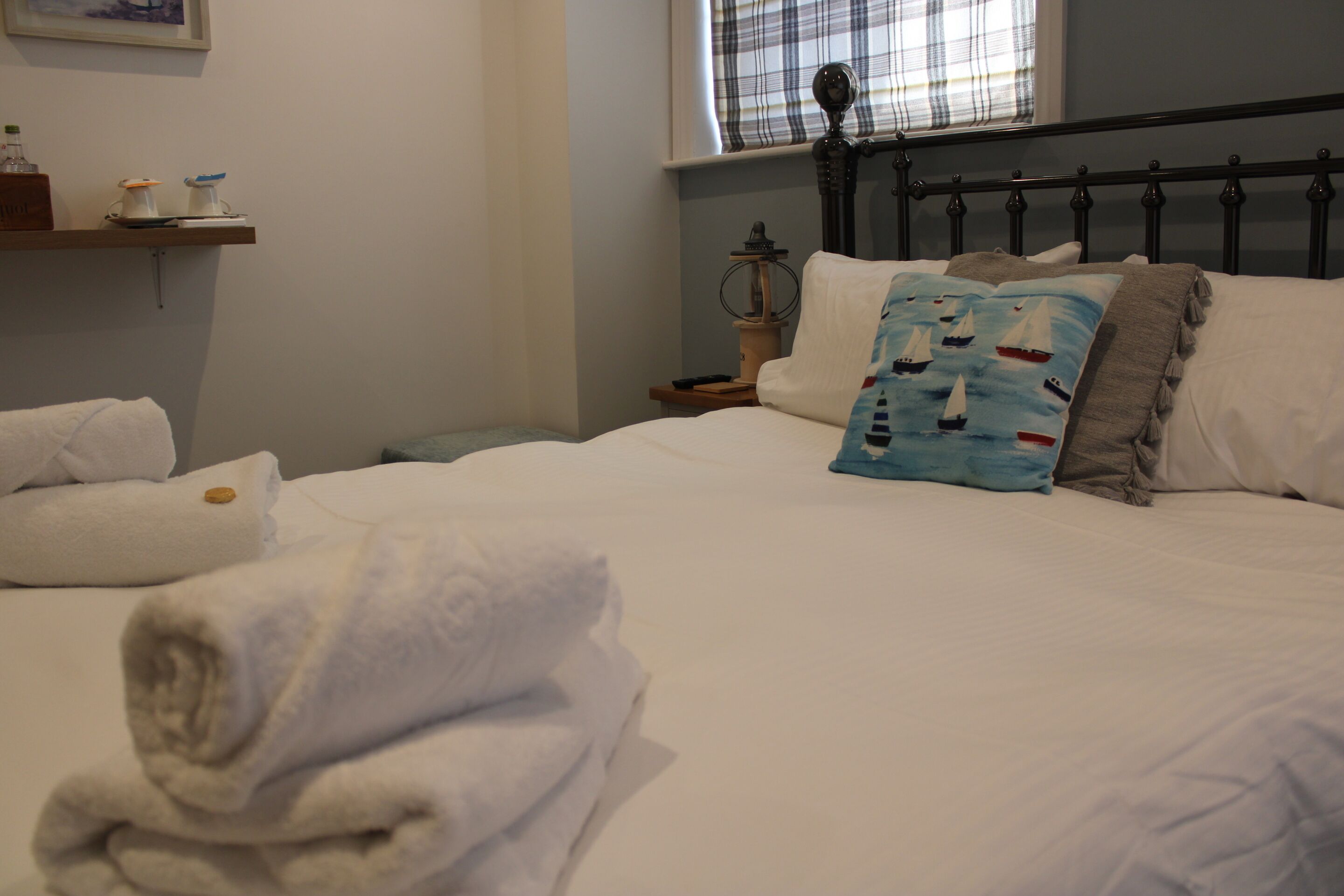 A neatly made bed with white linens and a blue pillow with sailboats.