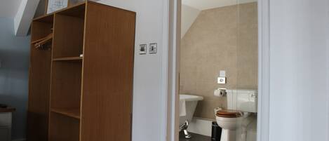 A bedroom with a wooden wardrobe, a bed, and a bathroom with a toilet and shower.