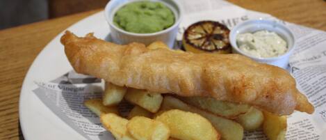 A plate of fish and chips with two small containers of sauces.