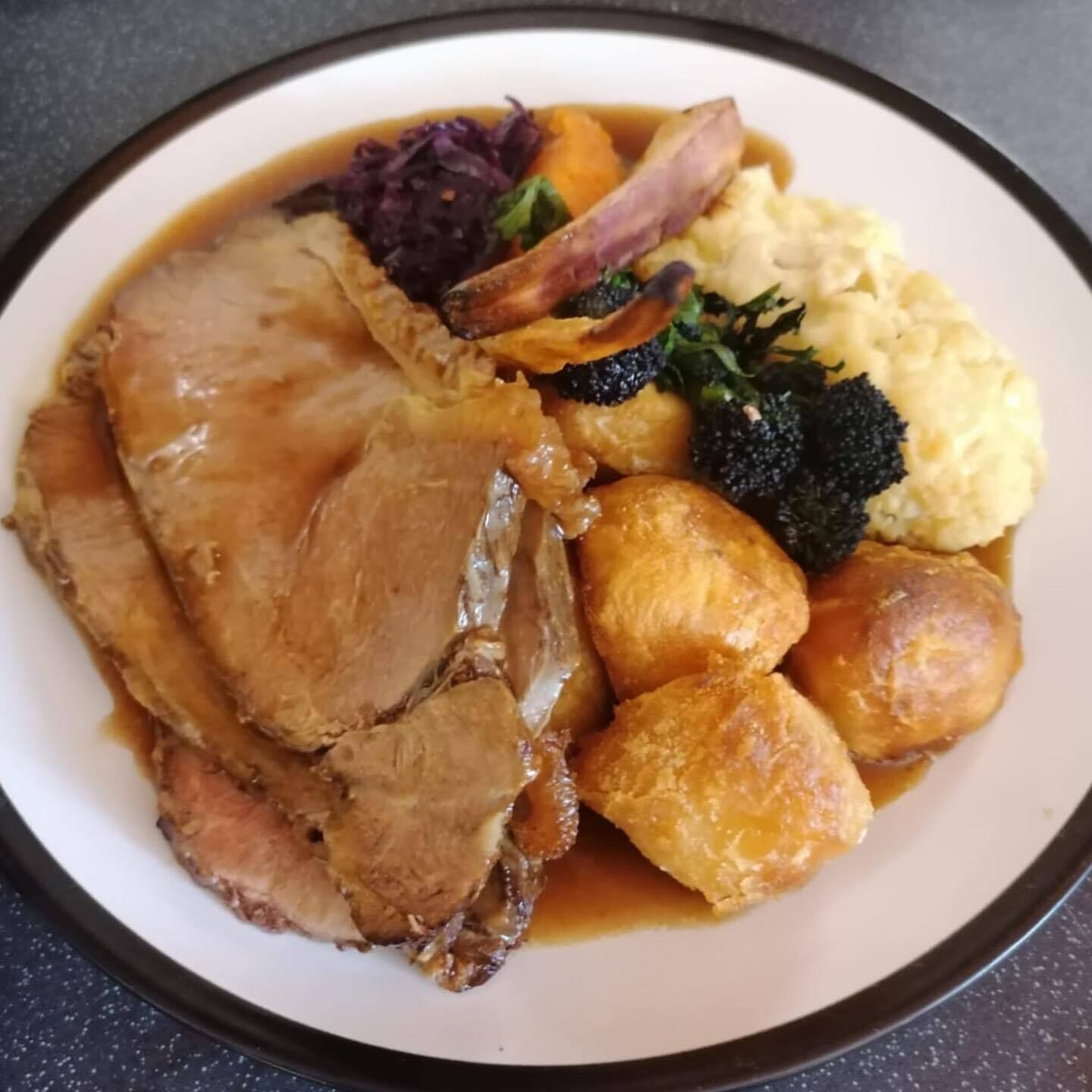 Ein Teller mit Braten, Yorkshire Pudding, Kartoffelpüree und Gemüse.