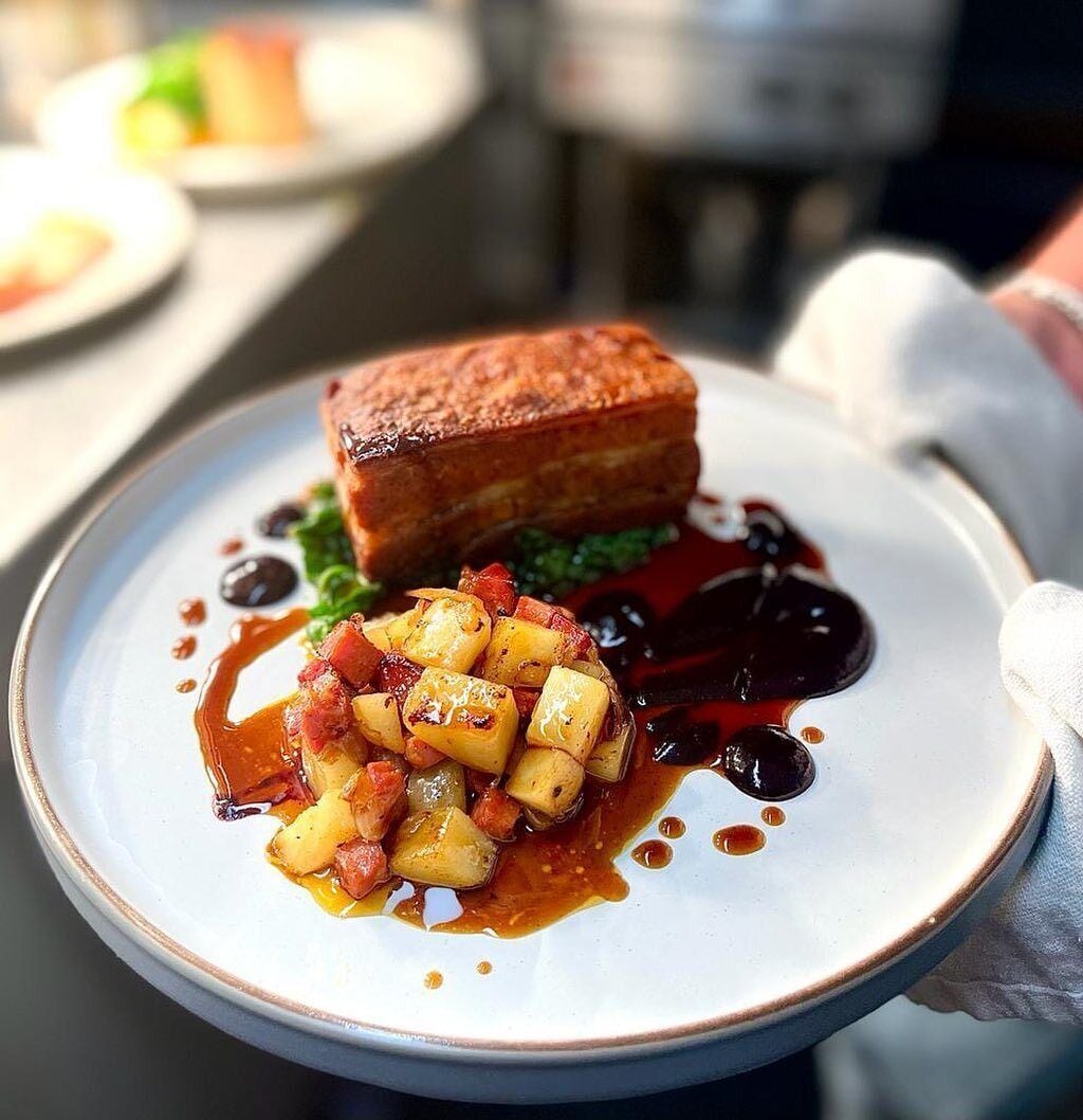 A plate with a piece of meat, diced potatoes, and a dark sauce.