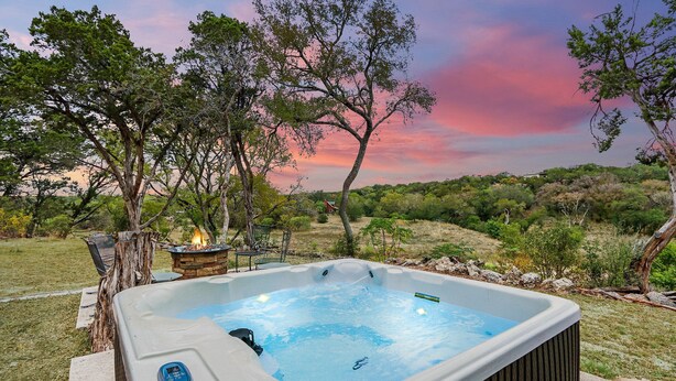 A hot tub with a fire feature, surrounded by trees and a scenic view. - Bungalow on the Bluff | Hot tub, Pet Friendly! (Wimberley)