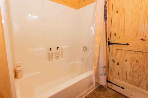A bathroom with a white bathtub, a wooden door, and a shower curtain.
