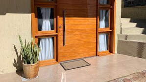 A wooden front door with two windows on each side, a potted plant, and a set of stairs leading to a balcony. - Loft Vale das Montanhas - Gramado - RS (Gramado)