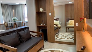 A modern living room with a sofa, a dining area, and a wooden partition with a mirror. - Loft Vale das Montanhas - Gramado - RS (Gramado)