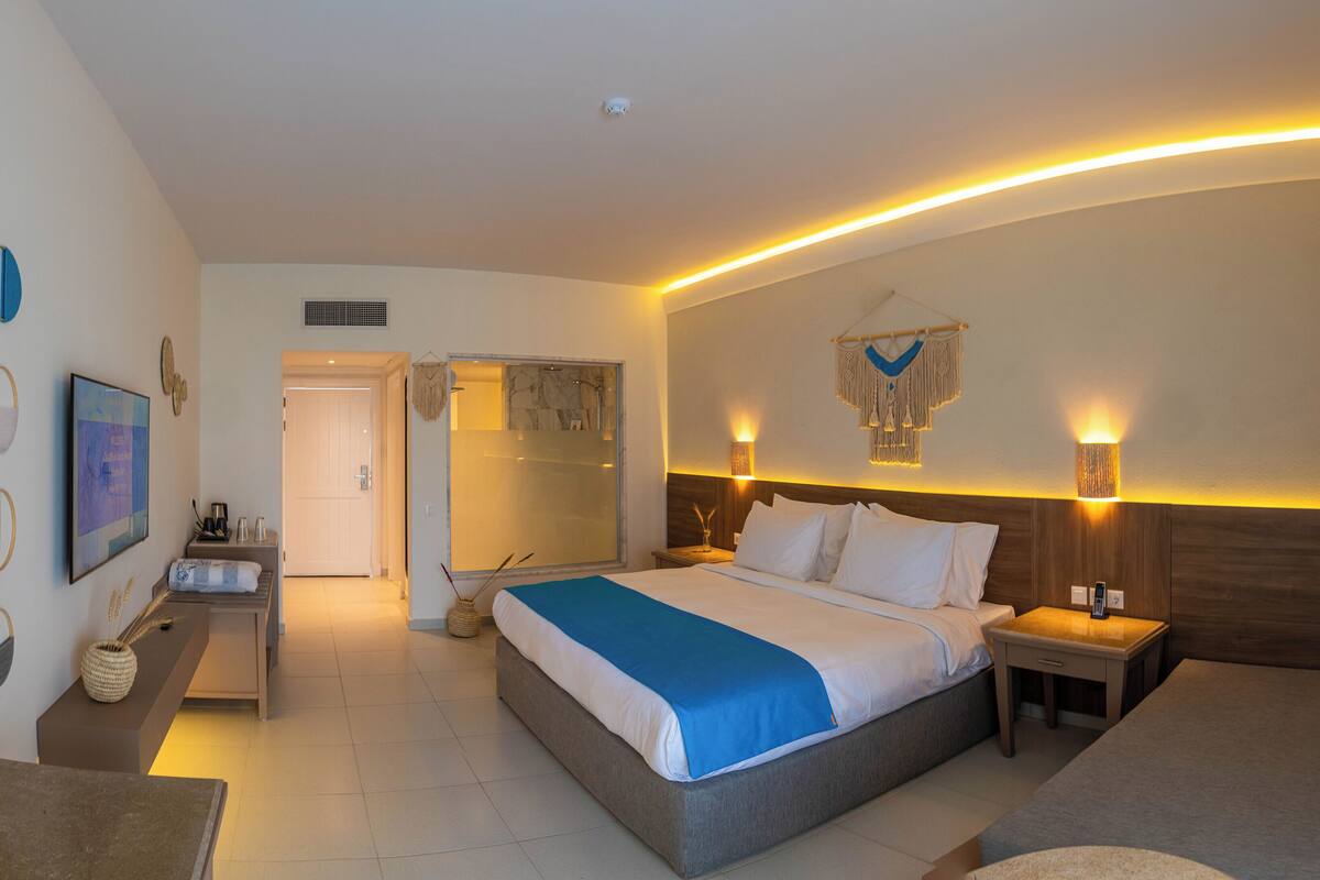 Quarto de hotel moderno com uma cama grande, mesas de cabeceira, um espelho e uma área de chuveiro.
