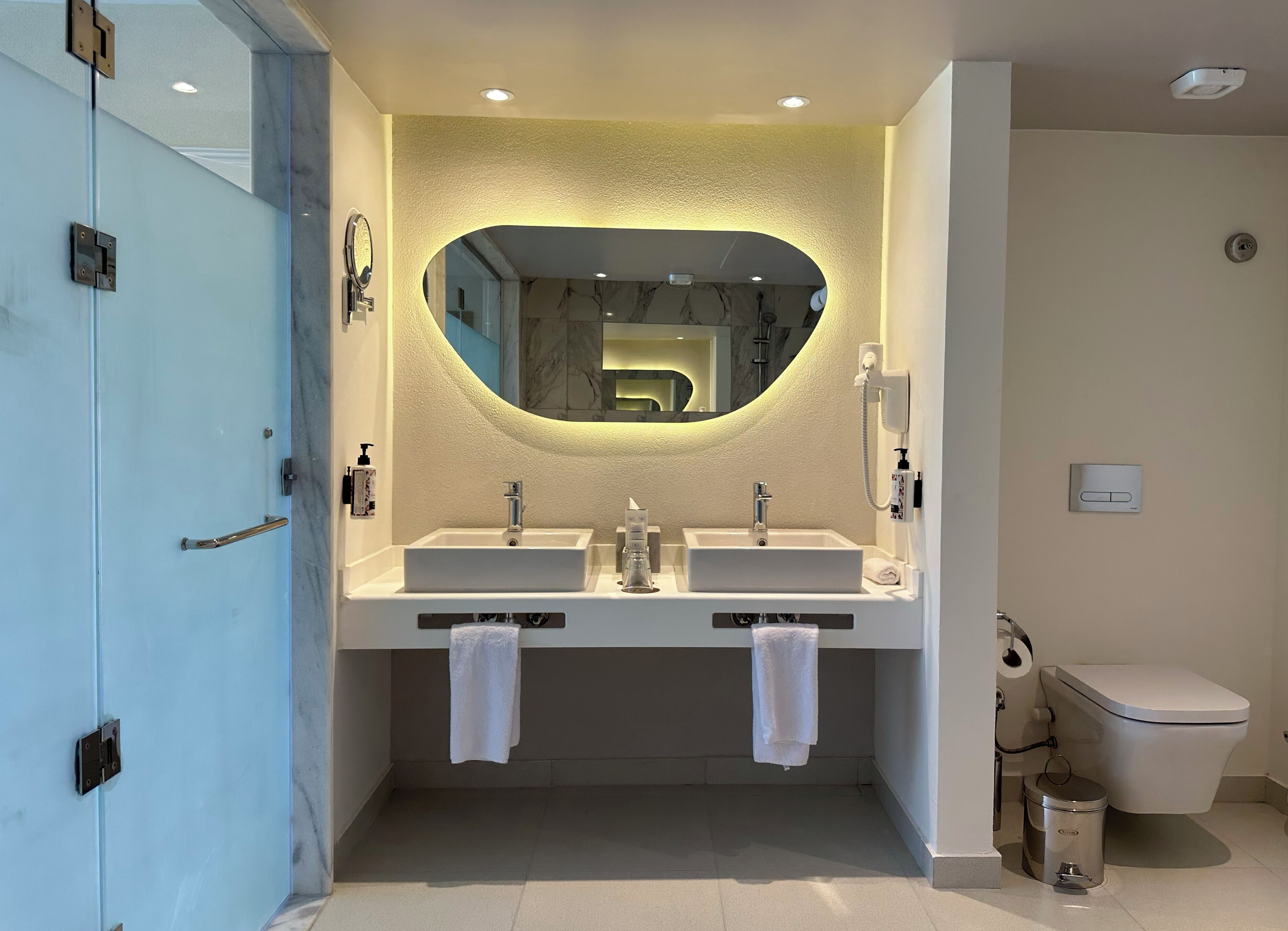 A modern bathroom with two sinks, a large mirror, and a toilet.