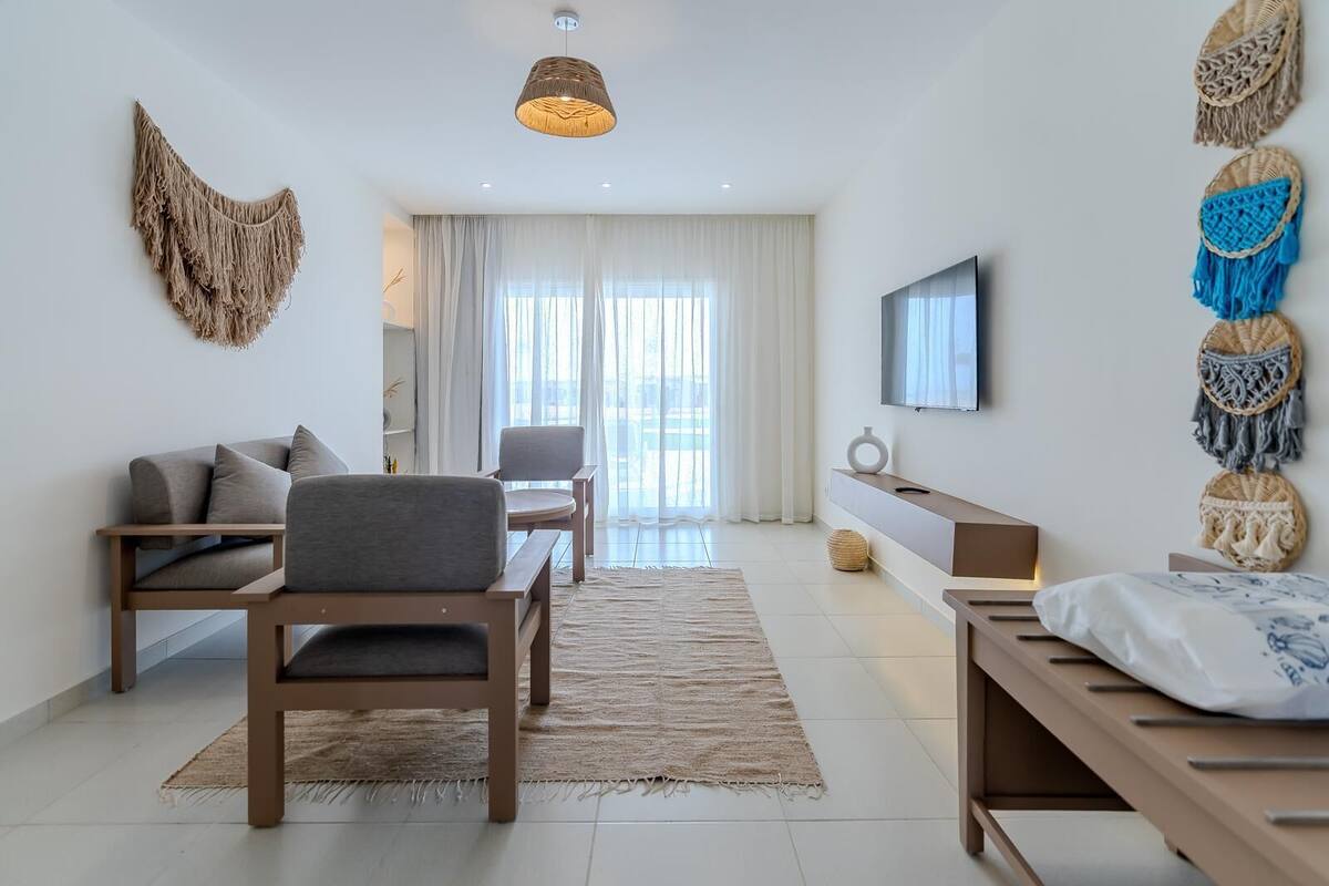 Uma sala de estar moderna com sofá, poltronas, TV e painéis de macramé decorativos.