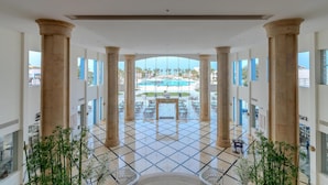 A hotel lobby with a view of a pool and palm trees, featuring columns and a tiled floor. - Casa Blue Resort (Marsa Alam)