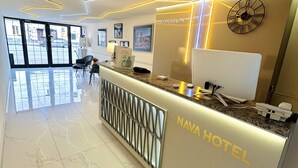 Zona de recepción de un hotel con piso de mármol, un mostrador de recepción que dice "NAVA HOTEL" y un reloj en la pared.