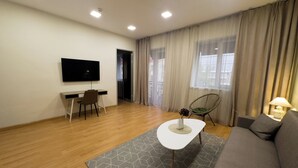 A modern living room with a flat-screen TV, a sofa, a dining table, and a chair. - NAVA Hotel Yerevan (Yerevan)