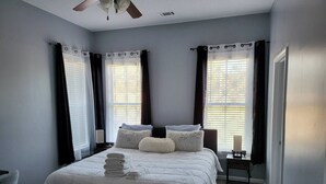 Een slaapkamer met een bed, twee nachtkastjes, een bijzettafeltje en een plafondventilator.
