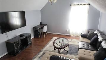 A living room with a flat-screen TV, a dark wooden entertainment unit, a leather sofa, a glass coffee table, and a ceiling fan.