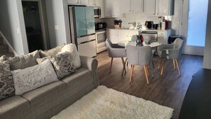 Een moderne keuken met witte kastjes, een koelkast en een eethoek met een glazen tafel en stoelen.