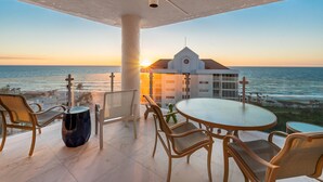 A balcony with a round table and chairs, overlooking the ocean at sunset. - Modern Condo Steps from the Private Beach with Amazing Views (Naples)