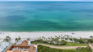 A beach view with clear turquoise waters, a sandy shore, and palm trees. - Modern Condo Steps from the Private Beach with Amazing Views (Naples)