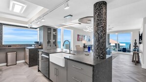 A modern kitchen with a large island, grey cabinetry, and a view of the ocean. - Modern Condo Steps from the Private Beach with Amazing Views (Naples)