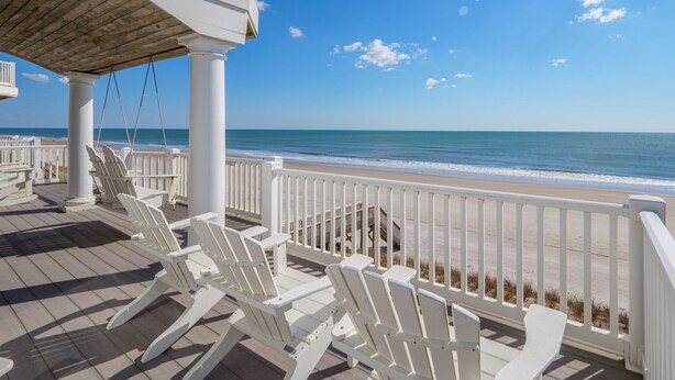 Eine Strandterrasse mit wei ßen Stühlen und einer Holzpergola mit Blick auf den Ozean.