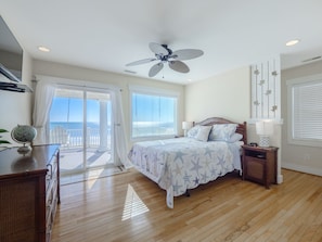 A bedroom with a bed, a nightstand, a dresser, a ceiling fan, and a view of the ocean through a sliding door. - Dolphin Parade #127 - Oceanfront, Hot Tub, Game Room, Sleeps #21! (North Topsail Beach)