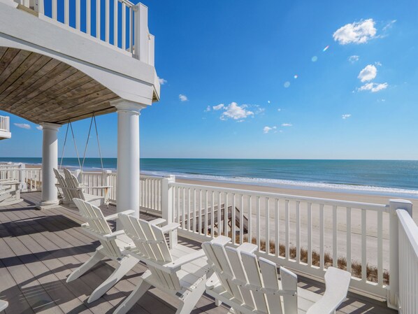 A beachside deck with white chairs and a wooden pergola overlooking the ocean.
