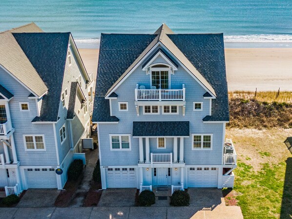 A two-story house with a balcony, a garage, and a driveway leading to the beach. - Dolphin Parade #127 - Oceanfront, Hot Tub, Game Room, Sleeps #21! (North Topsail Beach)