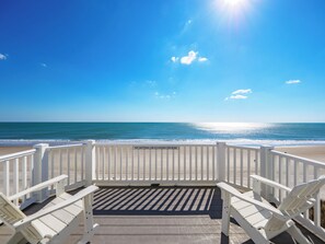 A beachside deck with white railings and lounge chairs facing the ocean.