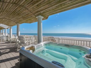 A covered outdoor area with a hot tub, white chairs, and a view of the beach. - Dolphin Parade #127 - Oceanfront, Hot Tub, Game Room, Sleeps #21! (North Topsail Beach)
