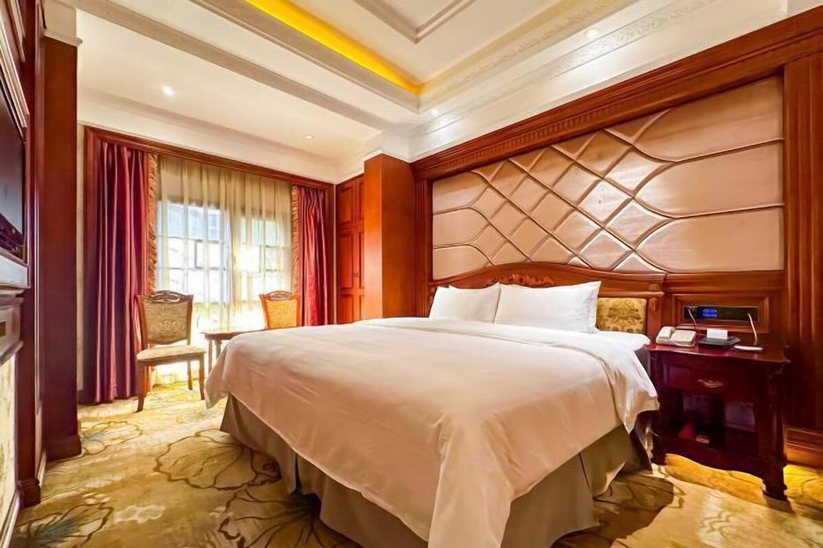 Une chambre d’hôtel avec un grand lit, une tête de lit en bois, une table de chevet avec un téléphone et une chaise.