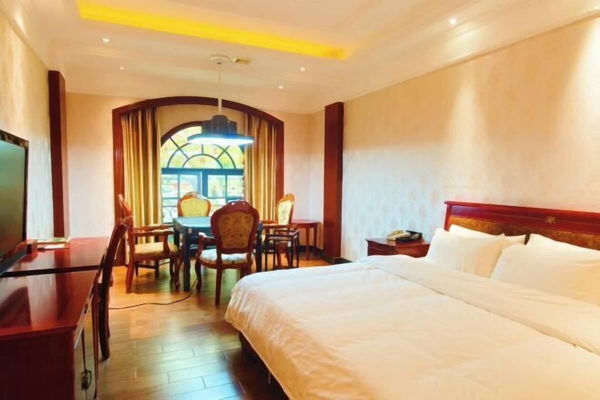 Une chambre d’hôtel avec un grand lit, un bureau avec des chaises, une télévision et une fenêtre avec des rideaux.