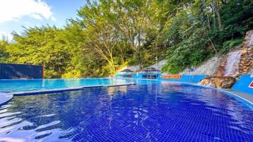 A swimming pool with clear blue water, surrounded by trees and a rocky hillside.