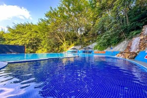 Une piscine à l’eau d’un bleu cristallin, entourée d’arbres et bordée d’une colline rocheuse.
