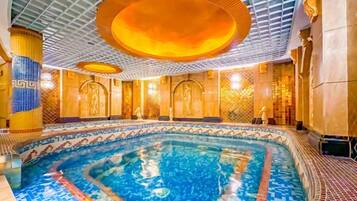 Una piscina interior con suelo de baldosas, zona central de natación y techo con diseño geométrico.