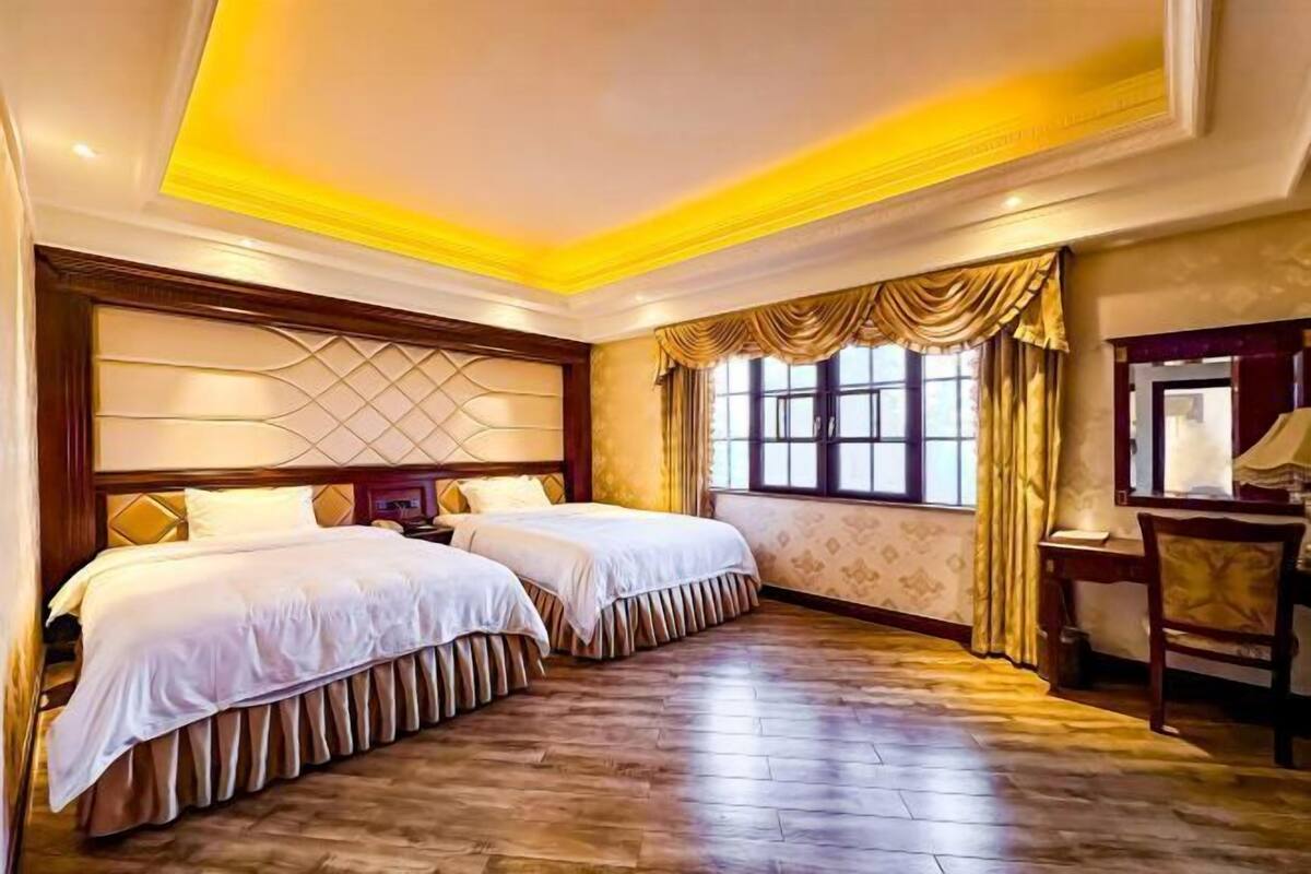 Une chambre d’hôtel avec deux lits, un plancher en bois, une grande fenêtre avec des rideaux et un bureau avec une chaise.