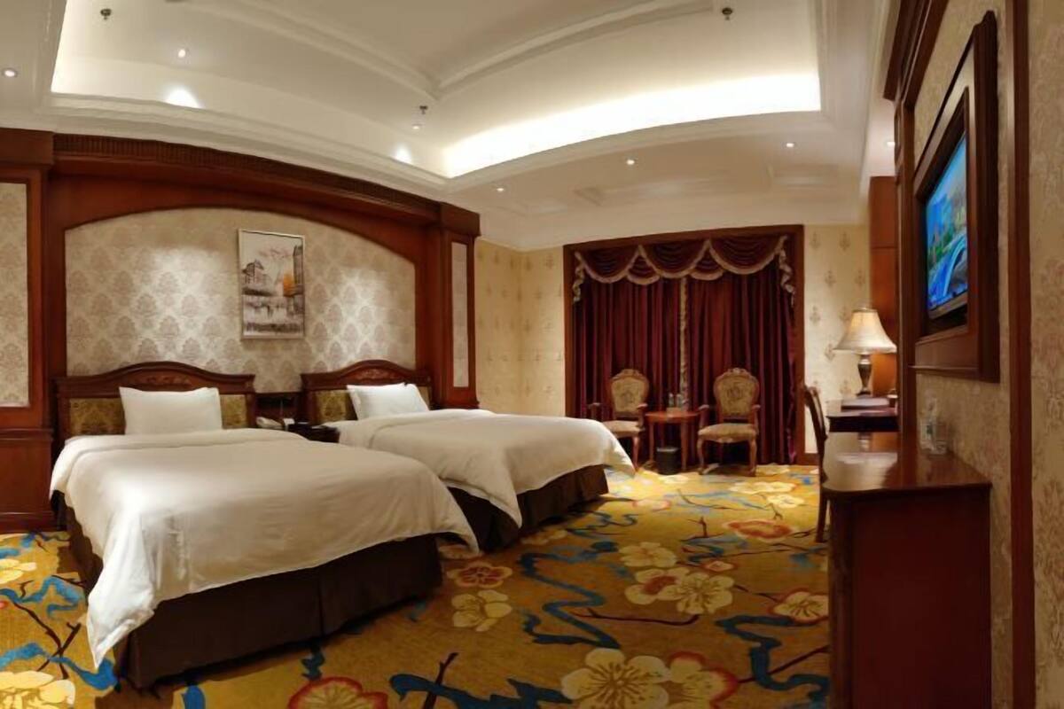 Une chambre d’hôtel avec deux lits, une grande moquette à motifs floraux, un téléviseur et un tableau au mur.