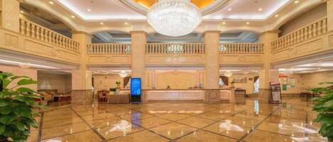 A spacious lobby with a large chandelier, a reception desk, and multiple balconies.