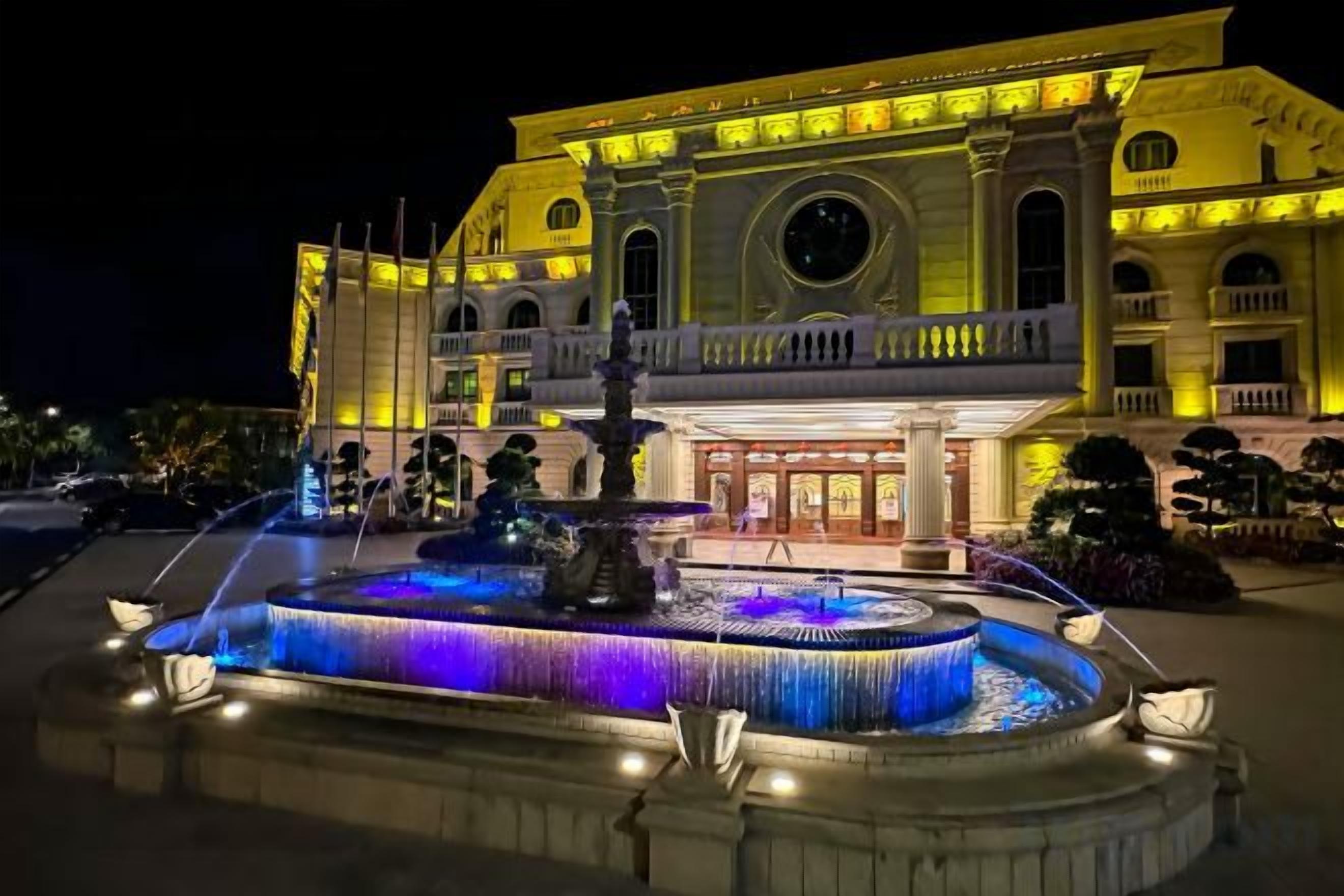 A grand hotel with a central fountain, a large circular window, and a balcony.