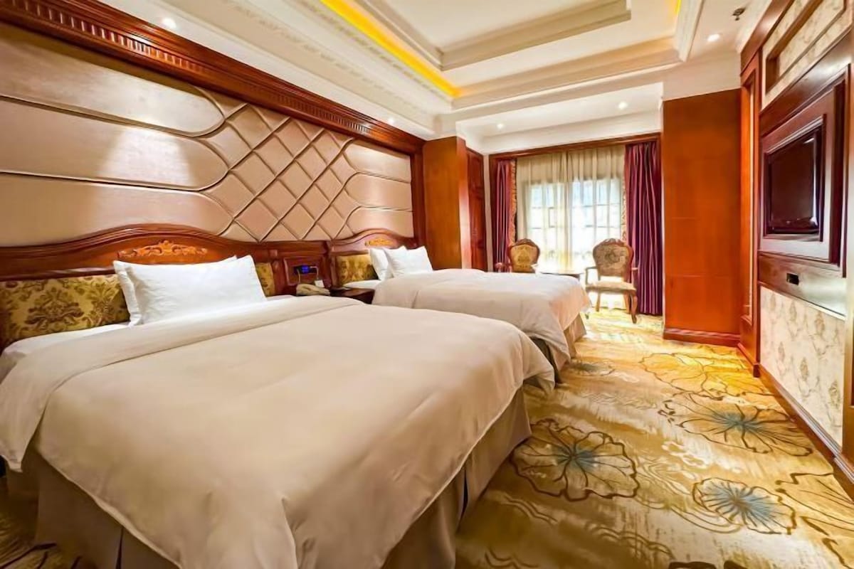 A hotel room with two beds, a large TV, and a floral carpet.