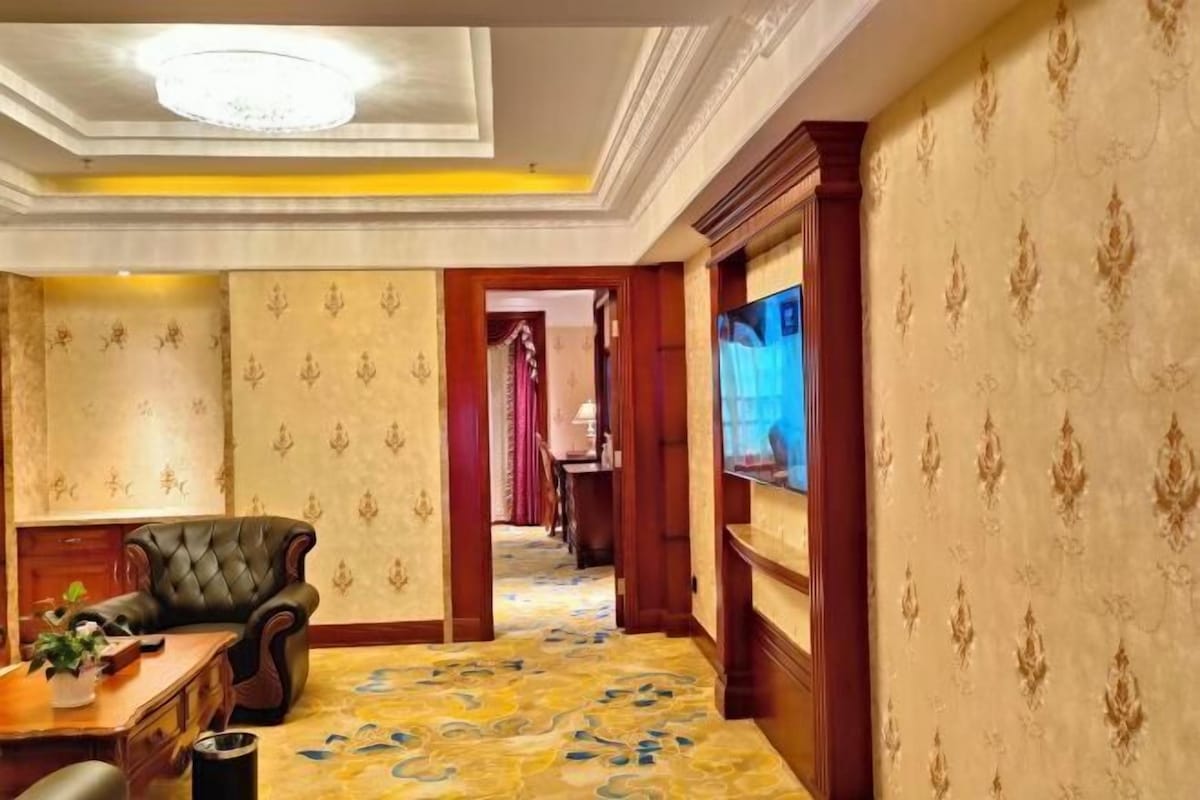 A room with a patterned carpet, a leather armchair, a wooden desk, and a television on the wall.