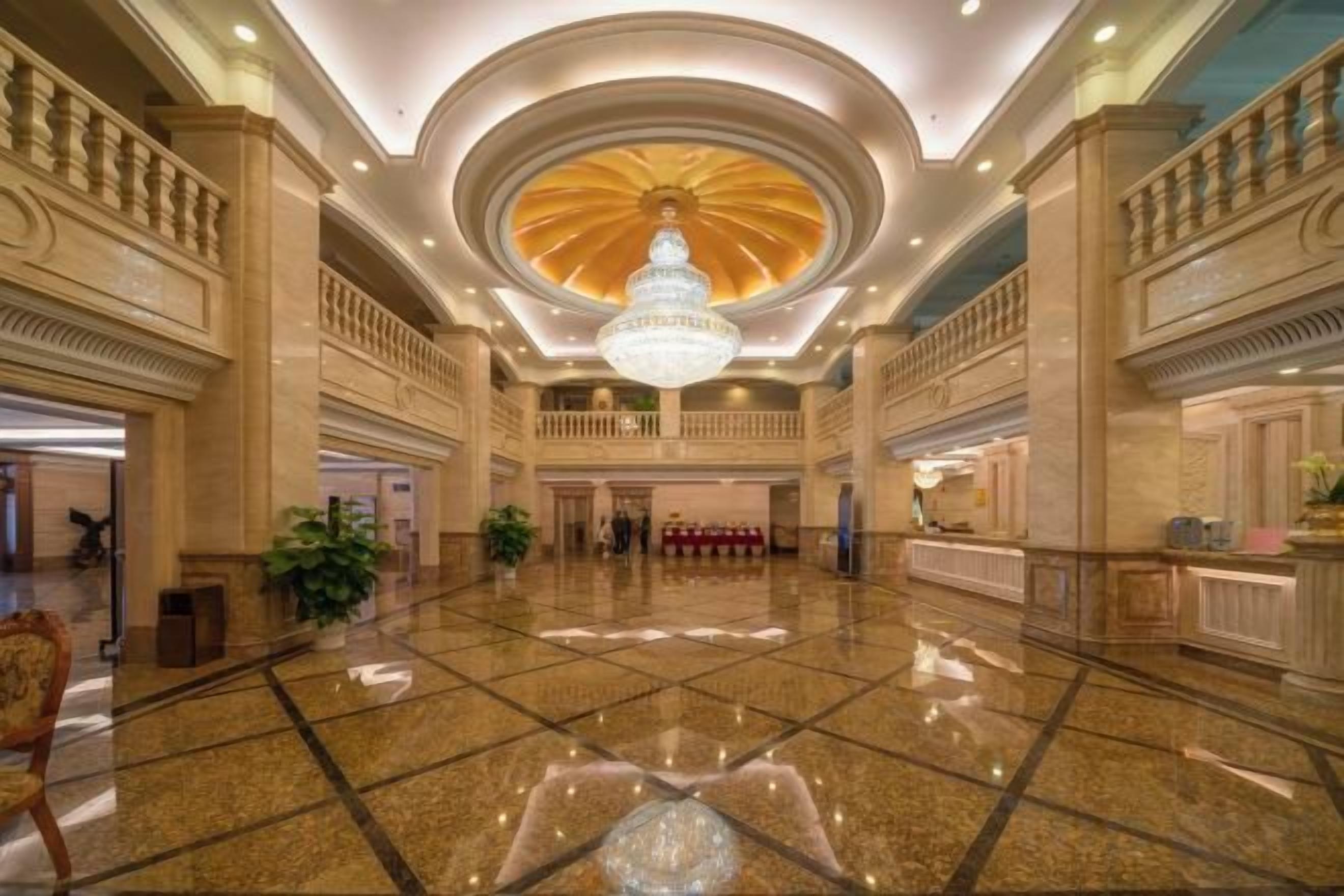 A spacious lobby with a grand chandelier, polished marble floors, and classical architecture.