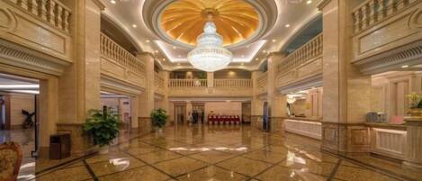 A spacious lobby with a grand chandelier, polished marble floors, and classical architecture.