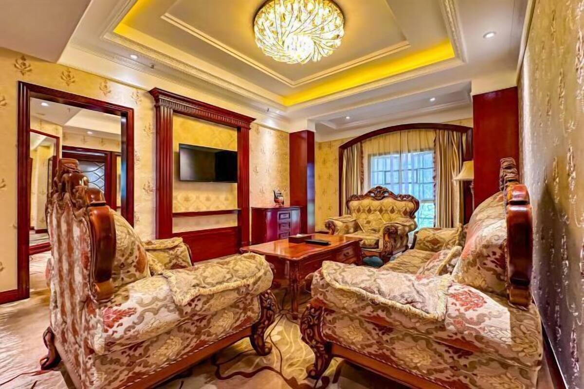 Un salon luxueux, agrémenté de meubles richement décorés, d’un lustre et d’un téléviseur.