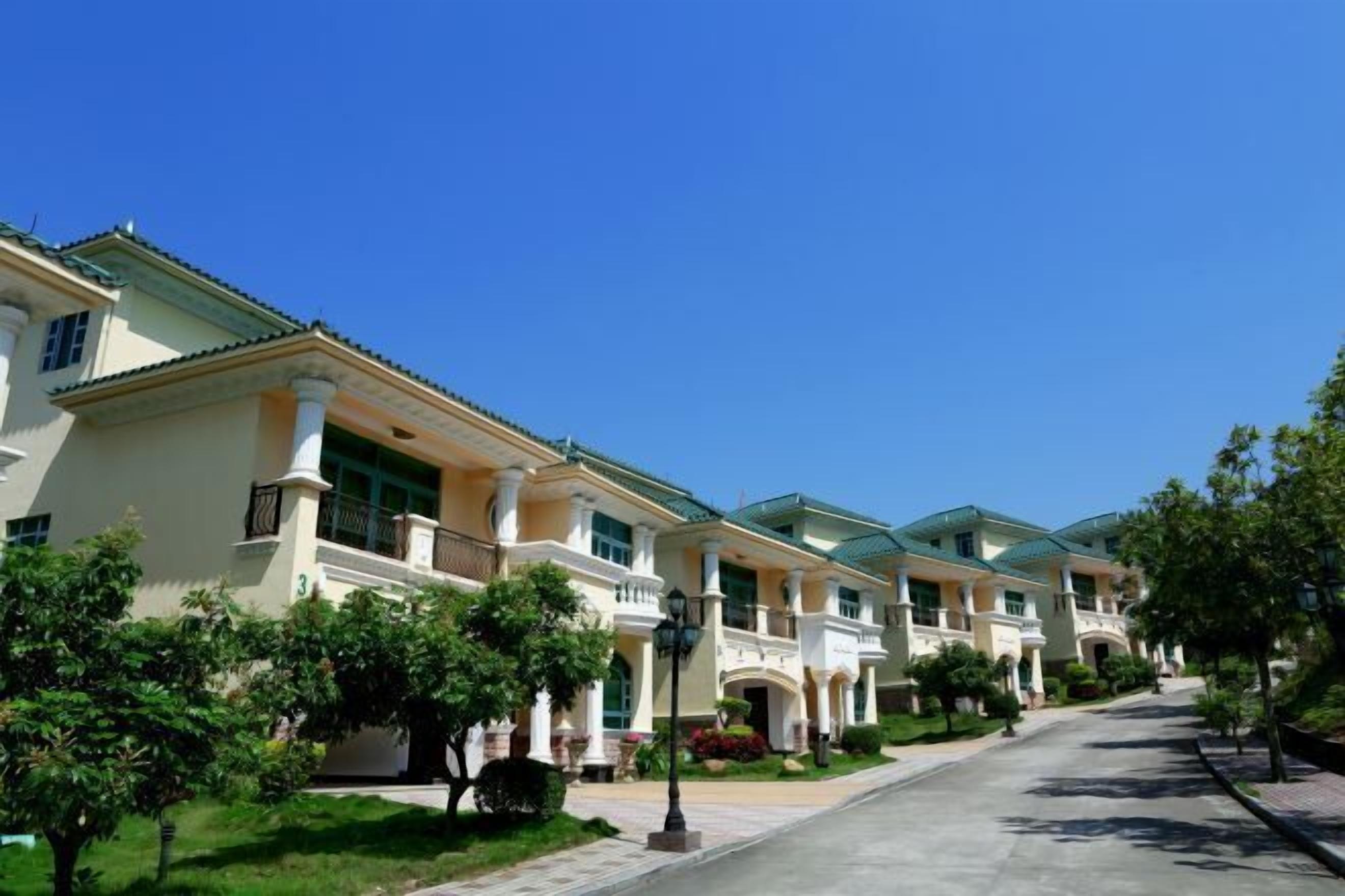 A row of modern, two-story houses with balconies, green lawns, and a clear blue sky.
