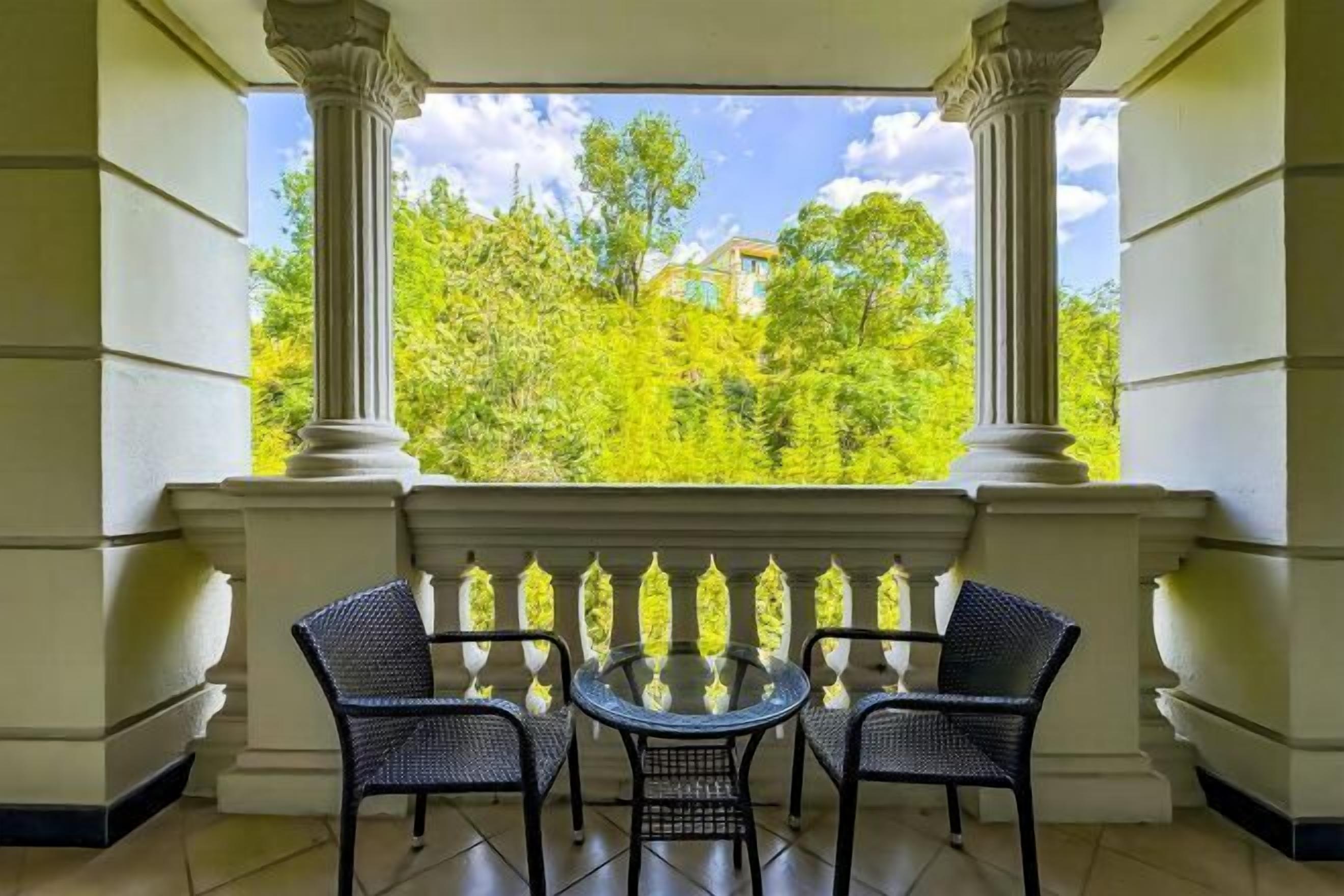 Un balcon avec deux fauteuils en osier et une table en verre, donnant sur un paysage verdoyant et luxuriant.