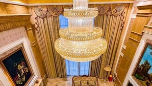 Een luxueuze kamer met een grote kroonluchter, decoratieve gordijnen, een bank en schilderijen aan de muur.