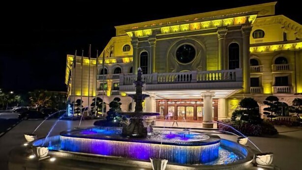 Een groot, verlicht gebouw met een centrale fontein en een verzorgde tuin.
