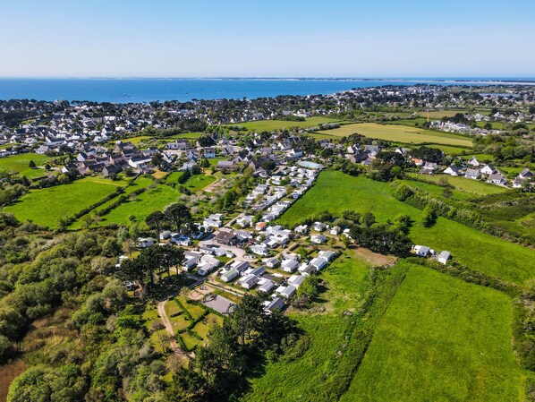 An aerial view of a residential area with houses, green fields, and a coastline. - Camping le Dolmen (Carnac)