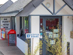 A reception area with a sign, a Coca-Cola vending machine, and a menu board outside a building. - Camping le Dolmen (Carnac)
